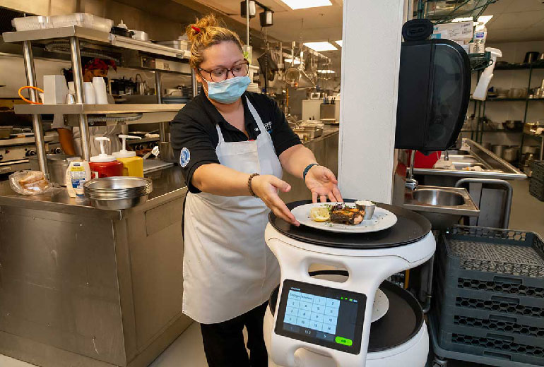 Robot chef wearing a covid mask placeing meal on a food delivery robot