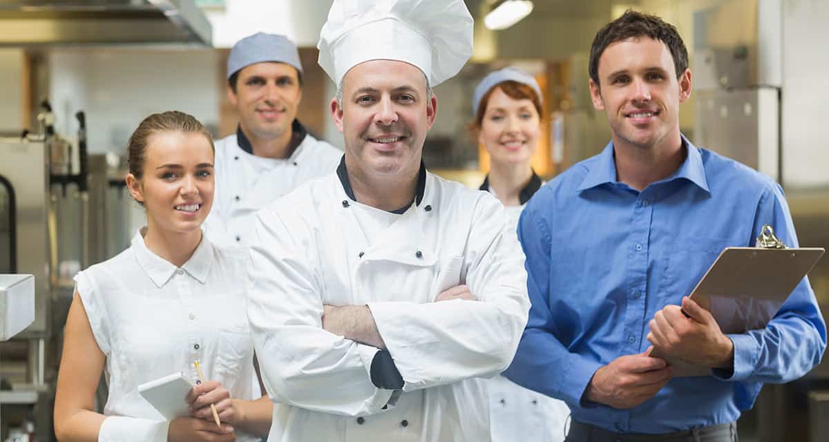 Just Get Started! Chef in white standing with kitchen staff looking at camera