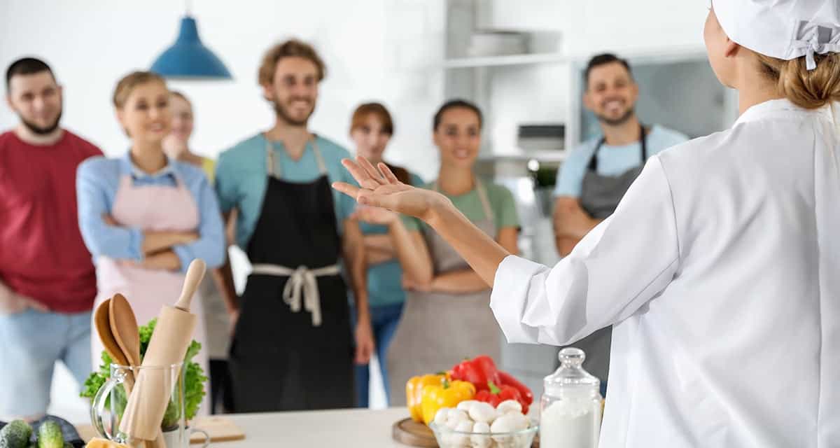 Just Get Started! Chef in white standing with kitchen staff looking at camera