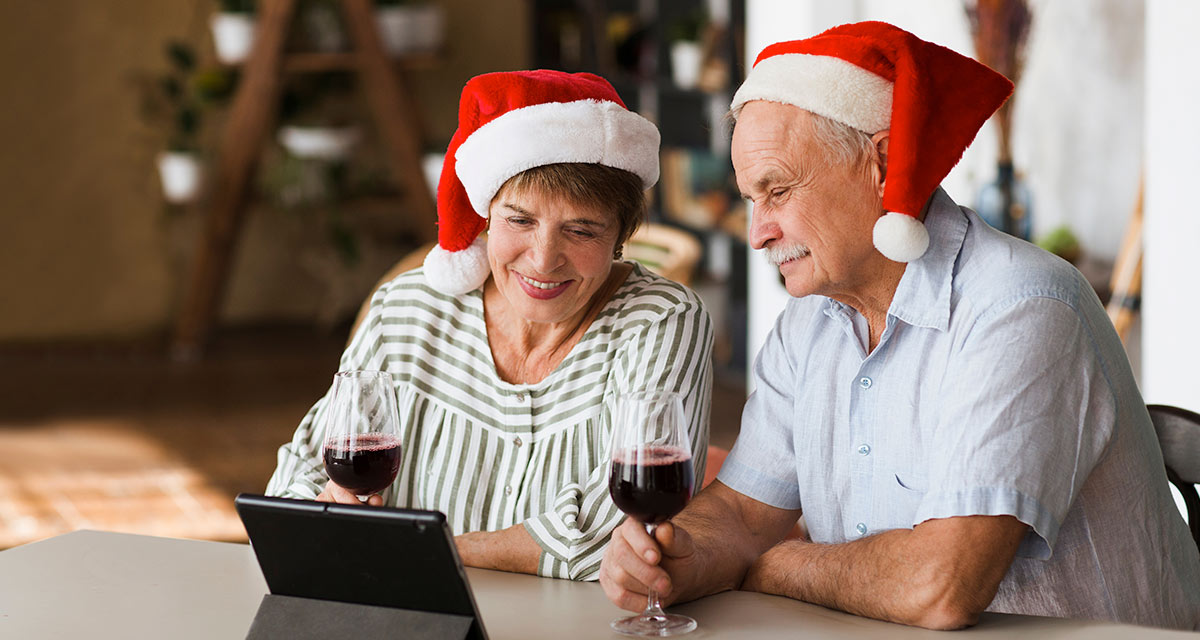 Christmas Couple Older couple wearing santa hats at christmas looking at tablet and drinking red wine