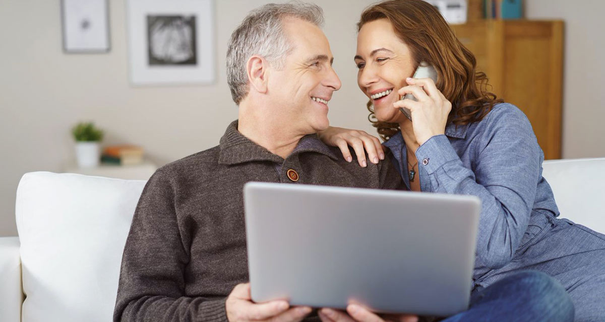 Family portals provide transparency and ongoing engagement Couple smiling on couch as they look on their computer and talk to family over the phone