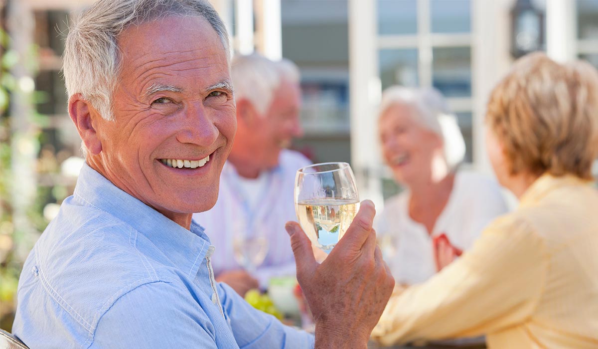 Senior Living POS Older man wearing a blue shirt at dinner with friends smiling while holding a glass