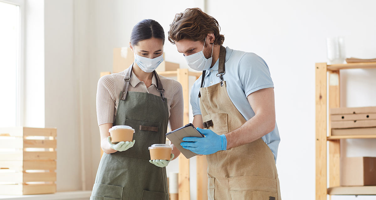 Software set them up for success Couple in apron wearing masks holding bowls and looking at tablet
